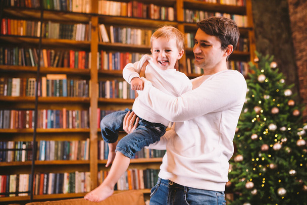 Happy young father and little son playing on Christmas evening at home. Playful dad and little boy have fun together at home on new year family winter holidays. Celebrate winter holidays at home. - Photo, Image