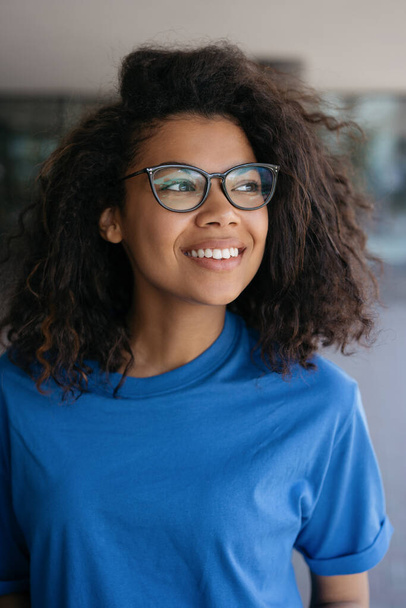 Young beautiful curly haired African American woman wearing stylish eyeglasses looking away outdoors. Portrait of pensive confident university student - Photo, Image
