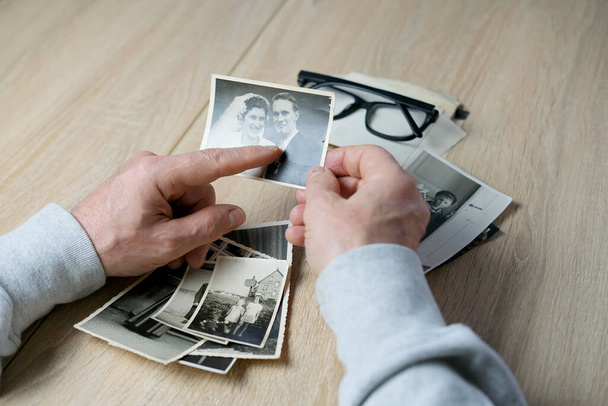 an elderly man looks through his old photographs of 1960-1965, the concept of nostalgia and memories of youth, childhood, remembering his life, relatives, family connection of generations - Фото, изображение