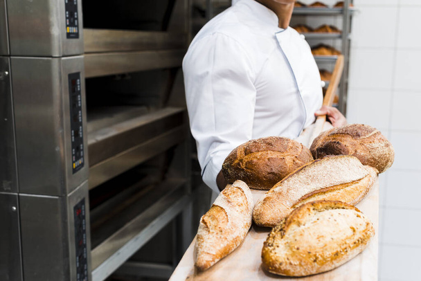 zbliżyć się mężczyzna piekarz gospodarstwa świeże pieczone chleb drewniana łopata z piekarnika. Wysokiej jakości zdjęcie - Zdjęcie, obraz