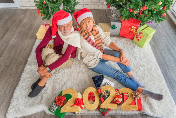 caucasian senior couple celebrate Christmas and 2022 New Year together with present and decorated Christmas tree at home - Fotografie, Obrázek