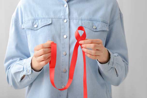 Kobieta trzymająca czerwoną wstążkę na jasnym tle. Koncepcja świadomości AIDS - Zdjęcie, obraz
