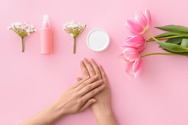 Female hands with cosmetic products and flowers on color background - Fotó, kép