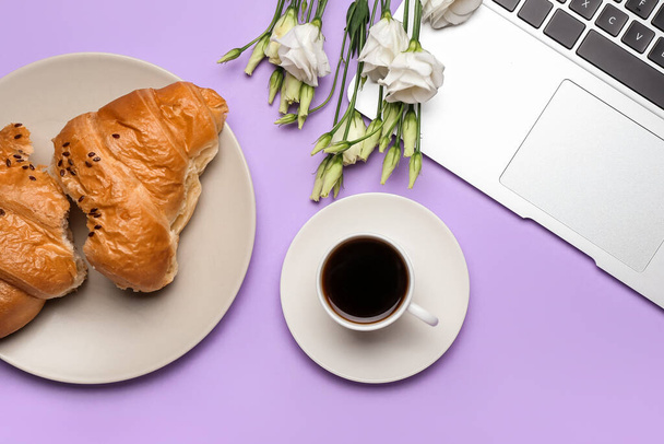 Cup of coffee, tasty croissant, laptop and flowers on color background - Fotó, kép