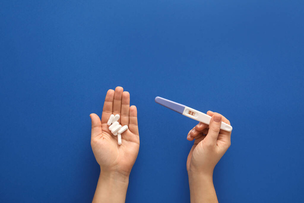 Manos femeninas con pastillas y prueba de embarazo sobre fondo de color - Foto, Imagen