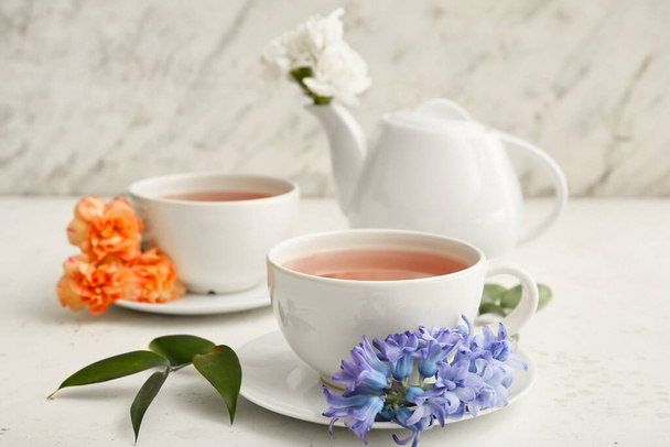 Teekanne und Tassen mit heißem Getränk mit Blumen auf dem Tisch - Foto, Bild