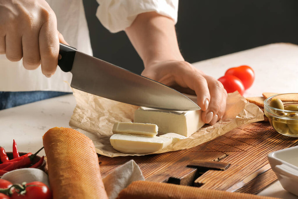 Woman cutting feta cheese on table in kitchen - Zdjęcie, obraz