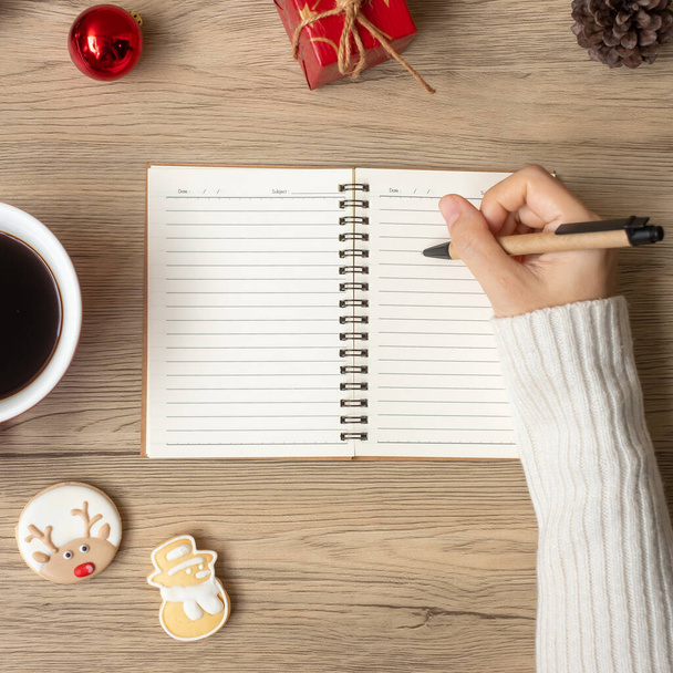 Vrouw handschrift op notitieboekje met zwarte koffiebeker en kerstkoekjes op tafel. Kerstmis, Gelukkig Nieuwjaar, Doelen, Resolutie, Lijst doen, Strategie en Plan concept - Foto, afbeelding