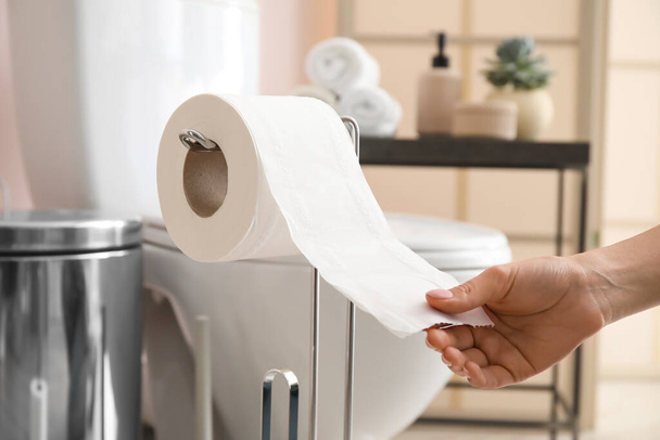 Frau reißt Toilettenpapier im modernen Badezimmer ab - Foto, Bild