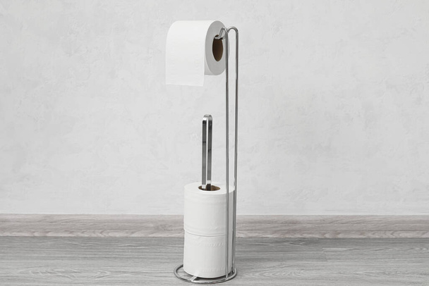 Support moderne avec rouleaux de papier toilette près du mur léger - Photo, image
