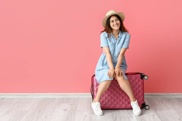 Νεαρή γυναίκα με βαλίτσα κοντά σε χρωματιστό τοίχο - Φωτογραφία, εικόνα