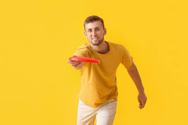 Przystojny młody człowiek rzuca frisbee na żółte tło - Zdjęcie, obraz