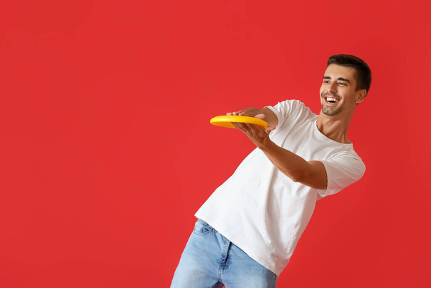 Schöner junger Mann fängt Frisbee auf rotem Hintergrund - Foto, Bild