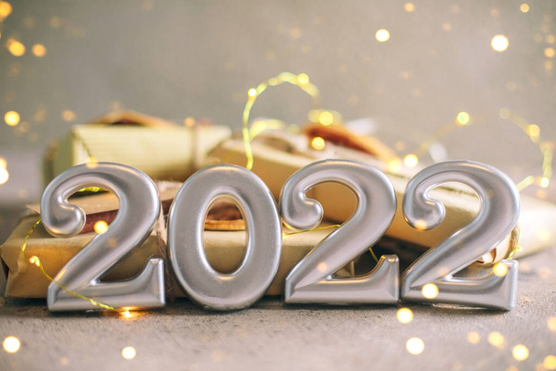 Christmas Greeting card. Number 2022 and stack of gift presents on holiday background. Christmas lights bokeh background. Happy New Year 2022, christmas, festive holiday concepts. Copy space - Φωτογραφία, εικόνα