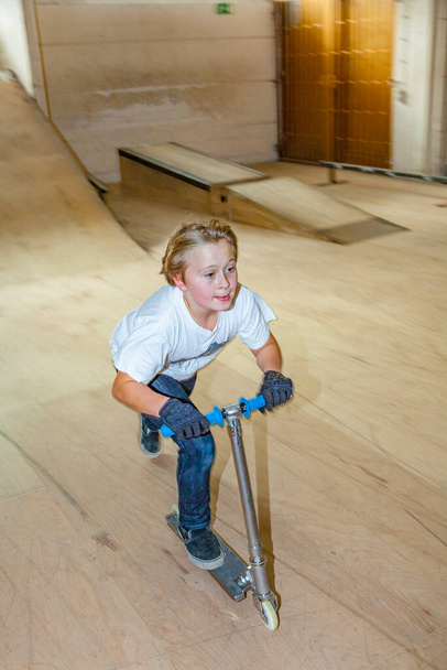 jongen scooting met zijn scooter in een skateboard hal - Foto, afbeelding