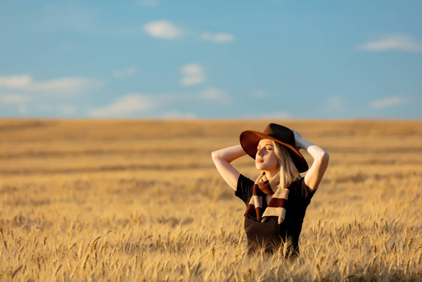 Blonde woman in black dress and hat with scarf in wheat field in autumn season time - Foto, imagen