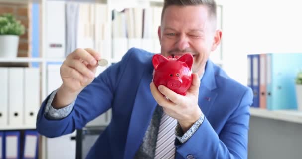 Jovem em terno de negócios jogando moeda em vermelho porquinho banco 4k filme - Filmagem, Vídeo