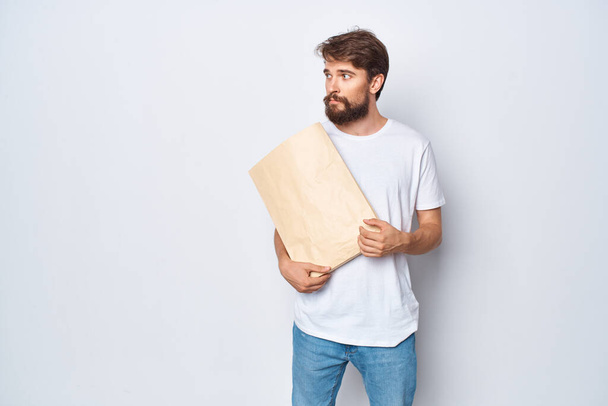 mies valkoisessa t-paidassa paperipussi kädessään kevyellä taustalla - Valokuva, kuva