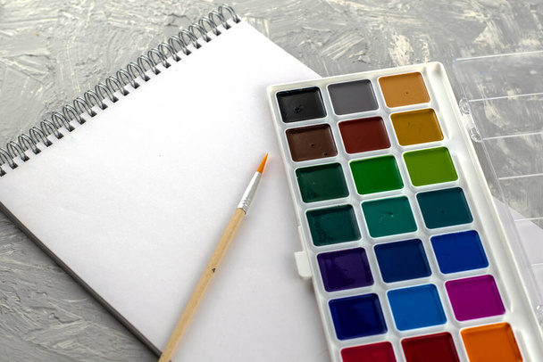 watercolor paints brush and sketchbook for drawing on a gray-white surface. High quality photo - 写真・画像
