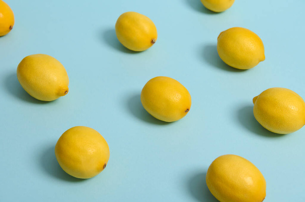 Creative summer food minimalistic background with raw ripe yellow bright lemons laid out in pattern on blue pastel surface. Copy space for ad. Studio shot with soft light - Fotoğraf, Görsel