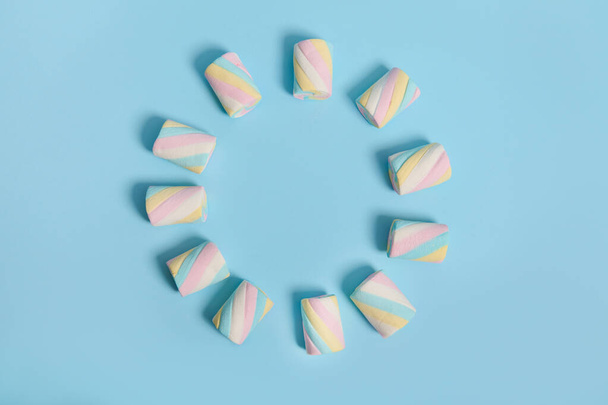 Coloridos malvaviscos dulces azucarados multicolores dispuestos en forma de círculo sobre un fondo azul pastel. Fondo alimenticio con espacio de copia para publicidad. Estilo minimalista, diseño - Foto, Imagen