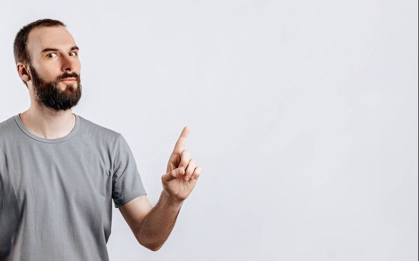 Portrait of cheerful young handsome man smiling looking at camera pointing finger upwards on white background with space for advertising mock up - Foto, afbeelding
