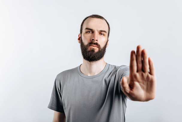 Portrait of handsome young man frowning while looking at camera holding hand opposite and saying stop gesture on white background with space for advertisement mock up - Photo, image