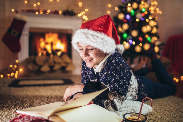 Niño leyendo un libro delante de un árbol de Navidad. - Foto, Imagen