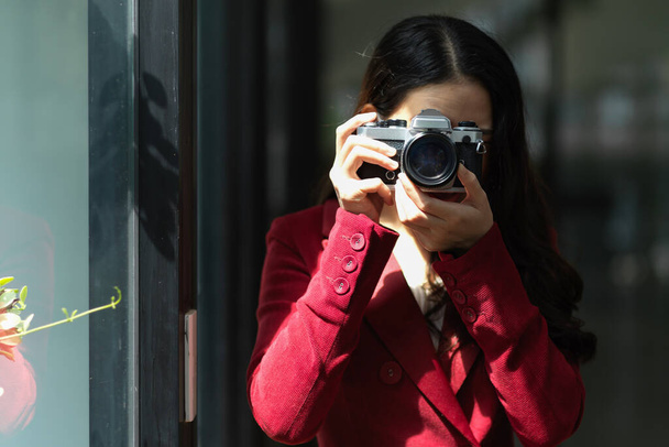 Young pretty female in a red suit with retro camera, taking picture, snap shot, focus the objects, hobby. - Φωτογραφία, εικόνα