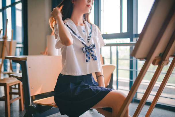 beautiful young woman in a white shirt and a skirt is sitting on the floor and looking at the camera - Photo, Image