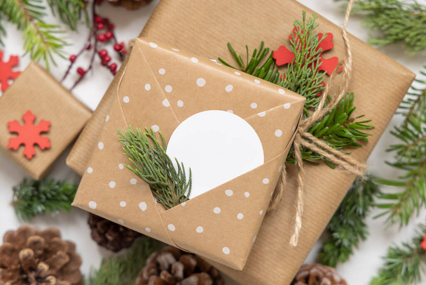 Christmas wrapped present with round paper gift tag with fir tree branches, pine cones and holiday decorations close up. Rustic winter composition with blank Gift tag Mockup, copy space, flat lay - Photo, Image