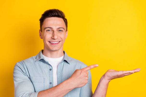 Photo of young cheerful good mood attractive guy advertising product offer isolated on yellow color background - Фото, зображення