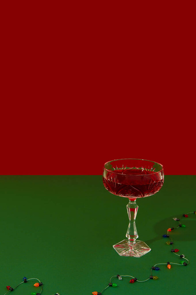 Christmas New Year creative composition with glass of red champagne and gerland on red and green background - Fotografie, Obrázek