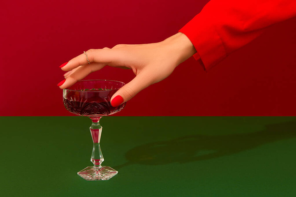 Christmas New Year creative composition with womans hand and glass of red champagne on red and green background - Foto, imagen