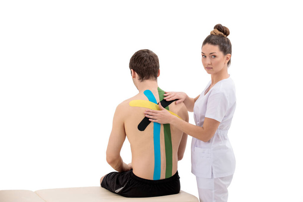 Female physiotherapist putting kinesiology tape on patients back isolated on white - Photo, image