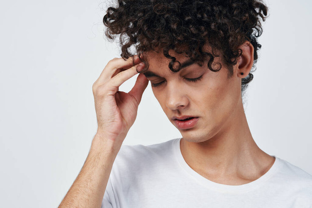 gars aux cheveux bouclés dans un t-shirt blanc migraine mécontentement - Photo, image