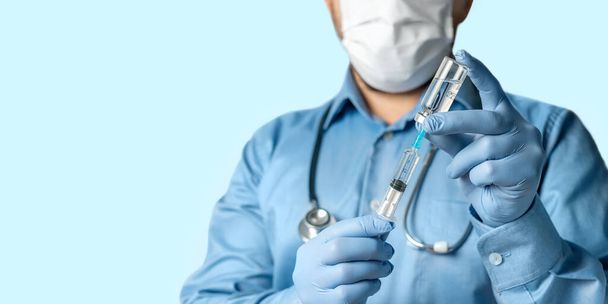Мужчина, доктор в голубой рубашке и перчатках, держит в руке шприц и бутылку вакцины против коронавируса или гриппа, концепция вакцинации. - Фото, изображение