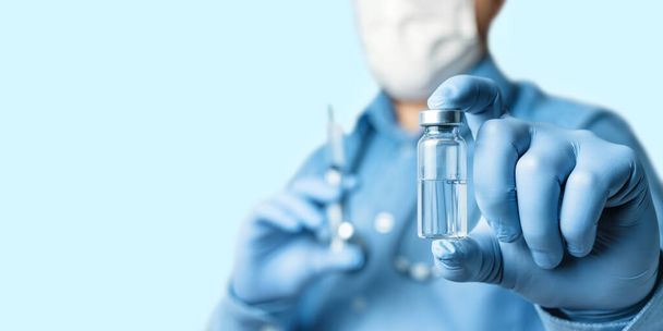 Muž, lékař v modré košili a rukavicích, drží v lahvičce vakcíny proti onemocnění koronavirem nebo chřipkou, vakcinační koncepce. - Fotografie, Obrázek