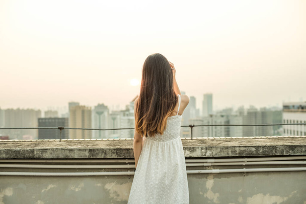 young woman in a white dress and a backpack on the roof of the city. - 写真・画像