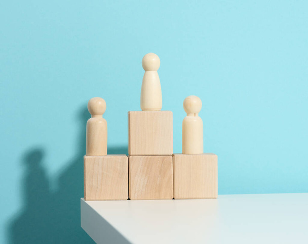 wooden figures of men stand on a pedestal of their cubes on a blue background. The concept of rivalry in sports, business and life. Achieving success and leadership - Photo, Image