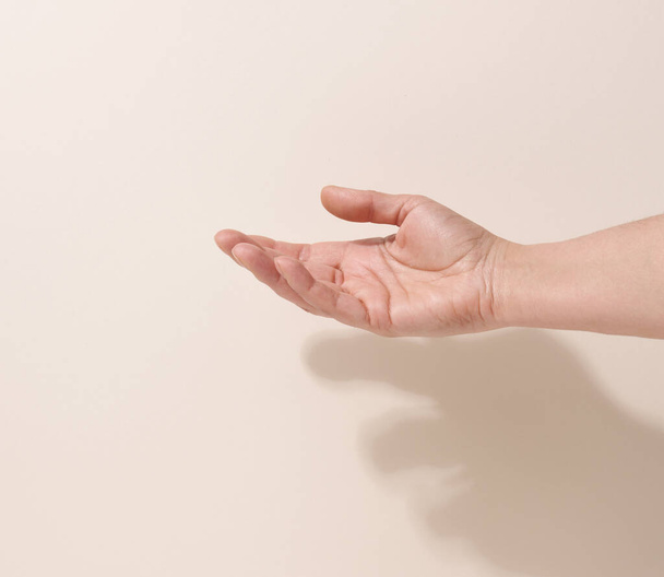 mano adolescente femenina para sostener algo sobre un fondo beige. Publicidad y promoción de productos - Foto, imagen