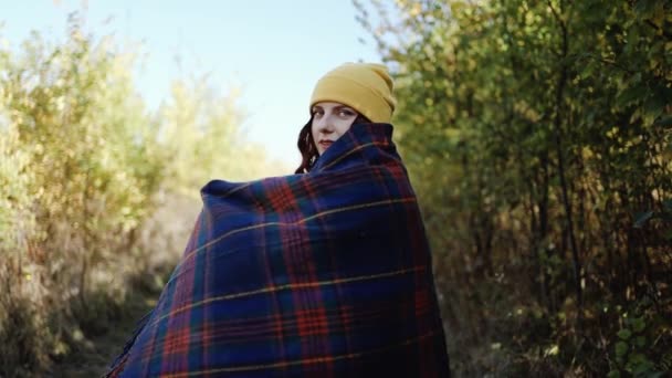 Kaukasische fröhlich lächelnde schöne junge Frau in heller stylischer Kleidung hüllt sich in ein blaues Wollkleid und genießt den sonnigen Herbst in der Natur im Wald - Filmmaterial, Video