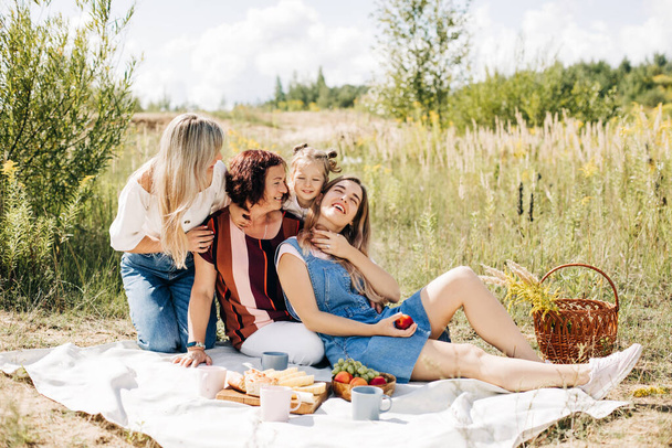 La familia está de picnic en el césped. Tres generaciones de mujeres de la misma familia descansan juntas - Foto, Imagen