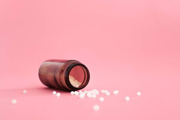 Zbliżenie obrazu homeopatycznych globulek w szklanej butelce na pastelowym różowym tle. Apteka homeopatyczna, ziołowa, medycyna naturalna, alternatywny lek homeopatyczny, opieka zdrowotna. Wolne miejsce, przestrzeń do kopiowania. - Zdjęcie, obraz