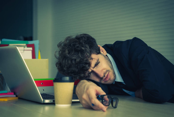 Hombre de negocios cansado tomando una siesta en su escritorio de trabajo en la oficina con computadora portátil y café para el concepto de oficina sobrecargado de trabajo. - Foto, Imagen