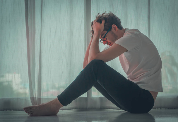 Homem caucasiano está sentado no chão pelas janelas com emoção deprimida por problemas e problemas. - Foto, Imagem