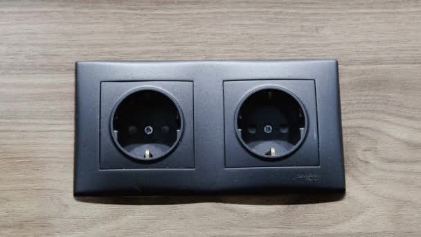Felame hand inserts the plug into electric socket. Grey plastic power socket and power plug on wood wall - Footage, Video