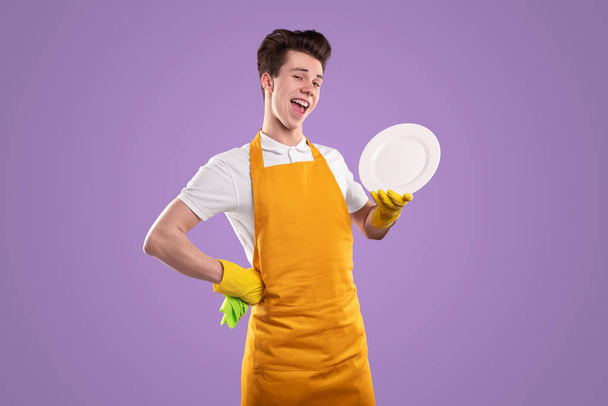 Content housekeeper with plate winking on violet background - 写真・画像