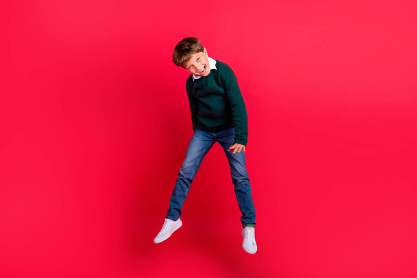 Photo of cute charming school boy wear knitted pullover smiling jumping high isolated red color background - Foto, Imagen