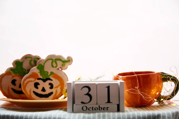 Happy Halloween still life with pumpkin cup and homemade cookies in shape of cute pumpkins and date of Halloween Day. Atmospheric aesthetic autumn holiday concept. Rural life. High quality photo - Photo, Image